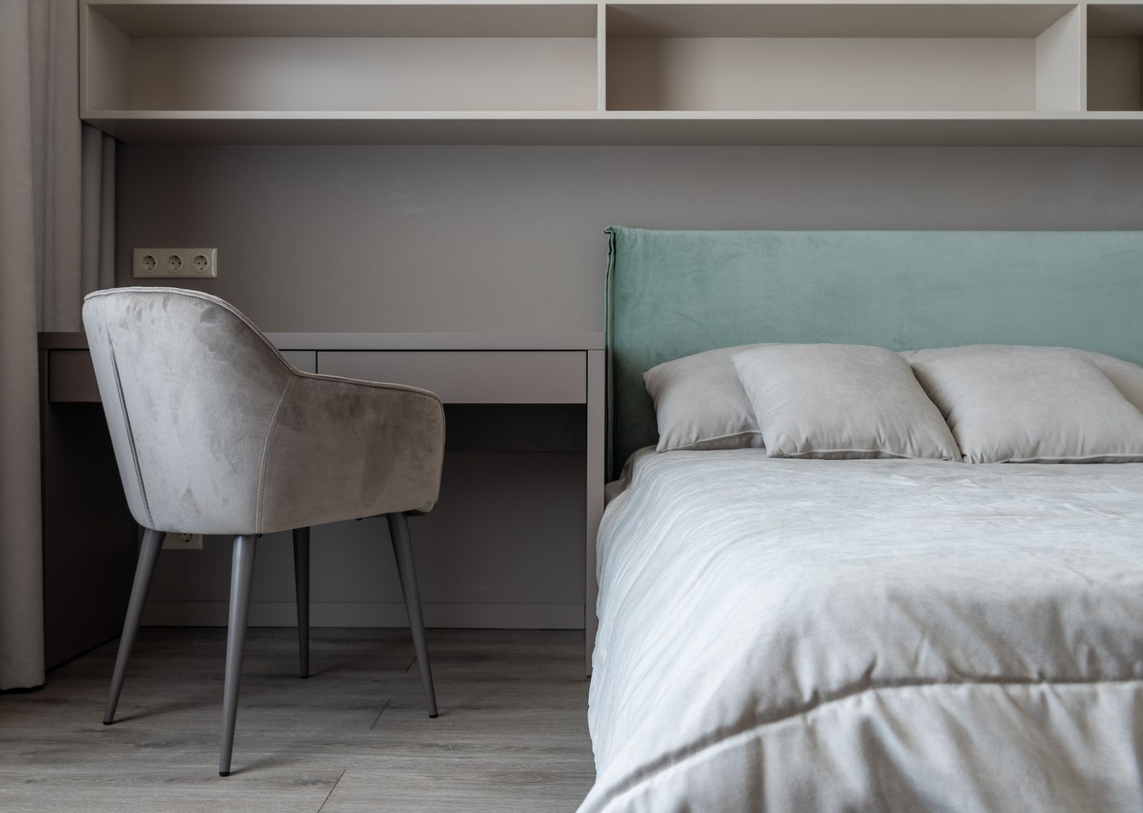 Standing desk against the wall of a small apartment bedroom with a walkway beside the bed