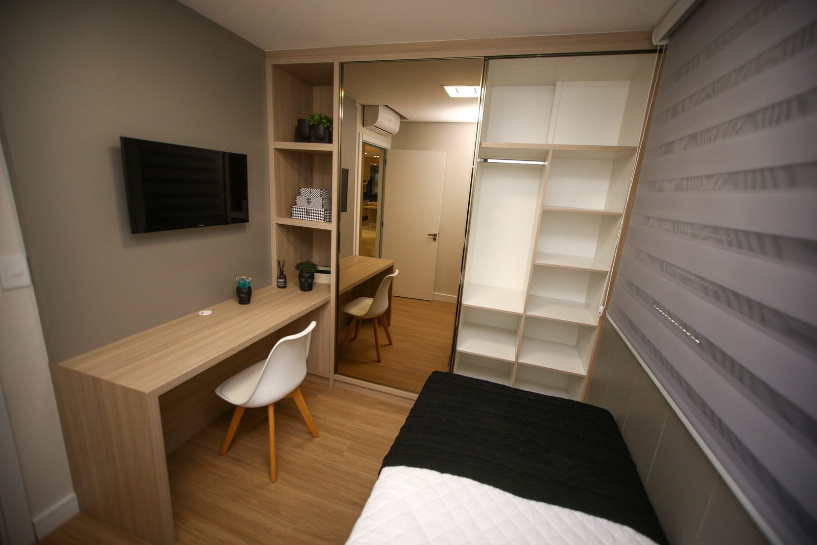 Wooden desk and chair placed beside a bed in a small bedroom