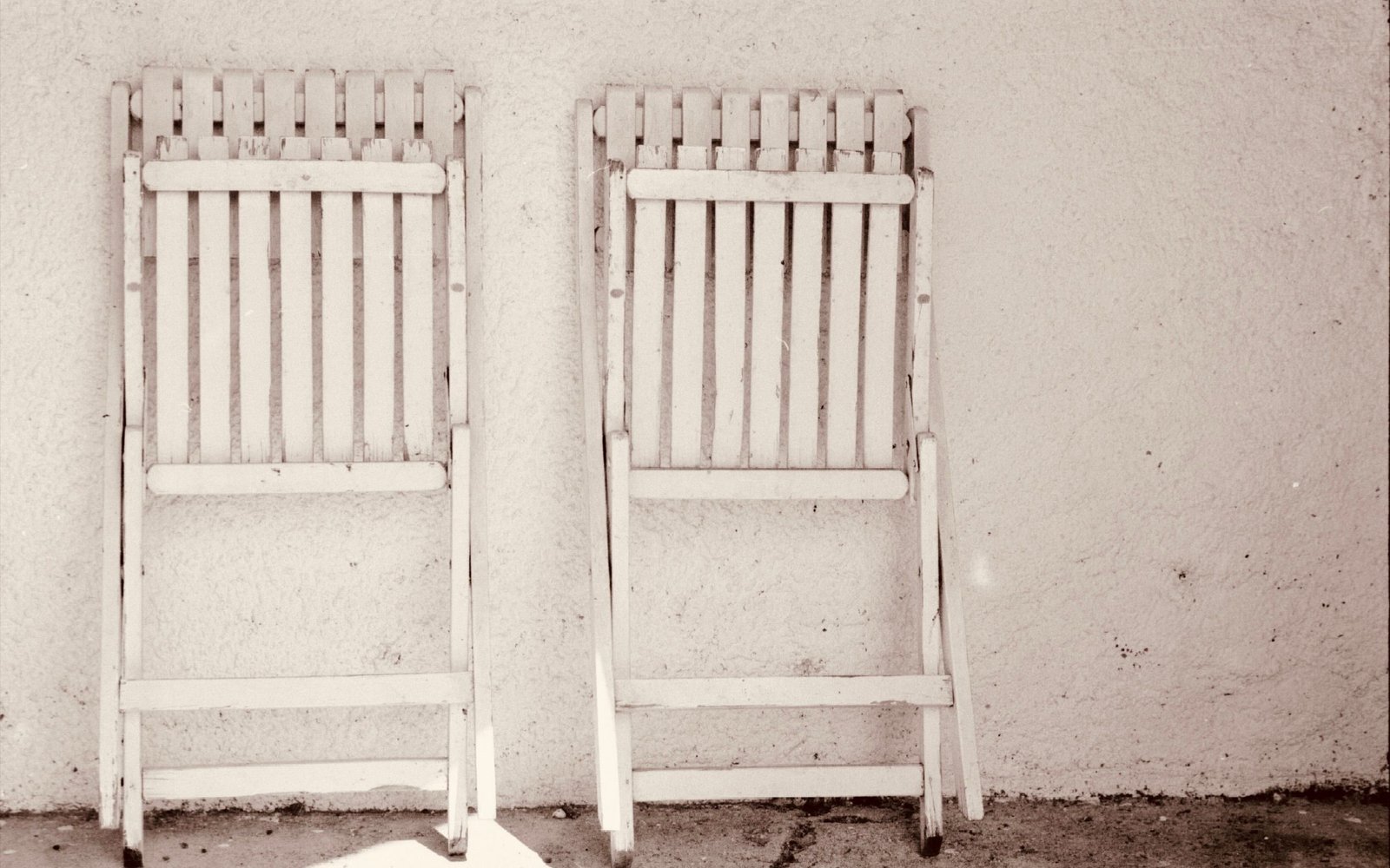 Two white slatted folding chairs leaning flat against a white wall, atmosphere photo, not a listing photo of any pick