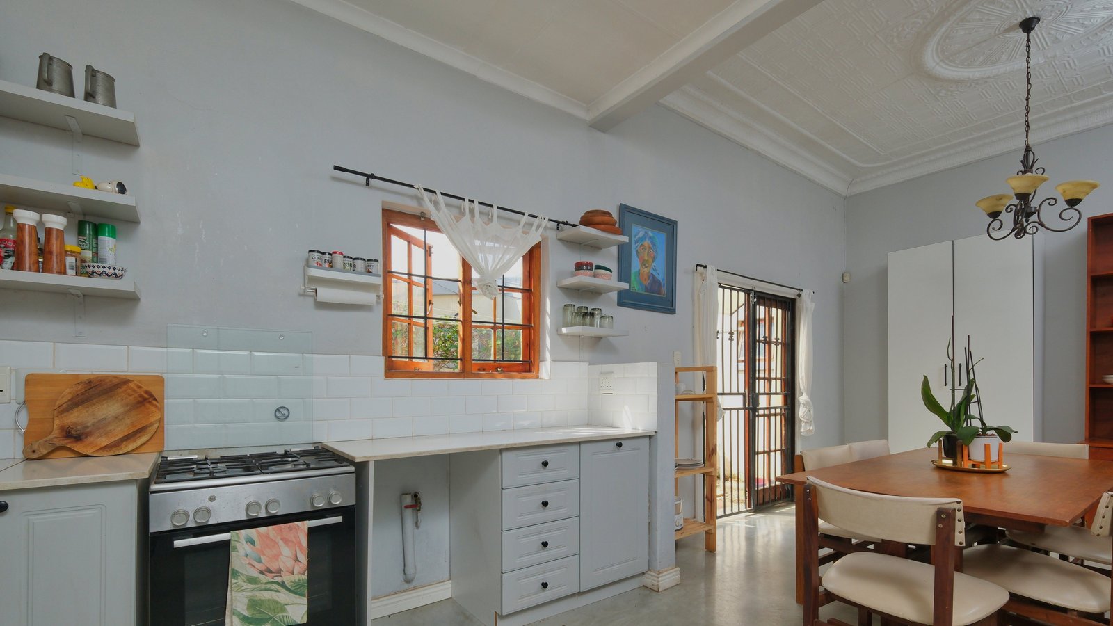 Small kitchen with a wooden dining table and chairs beside the stove and a window, atmosphere photo, not a product pick