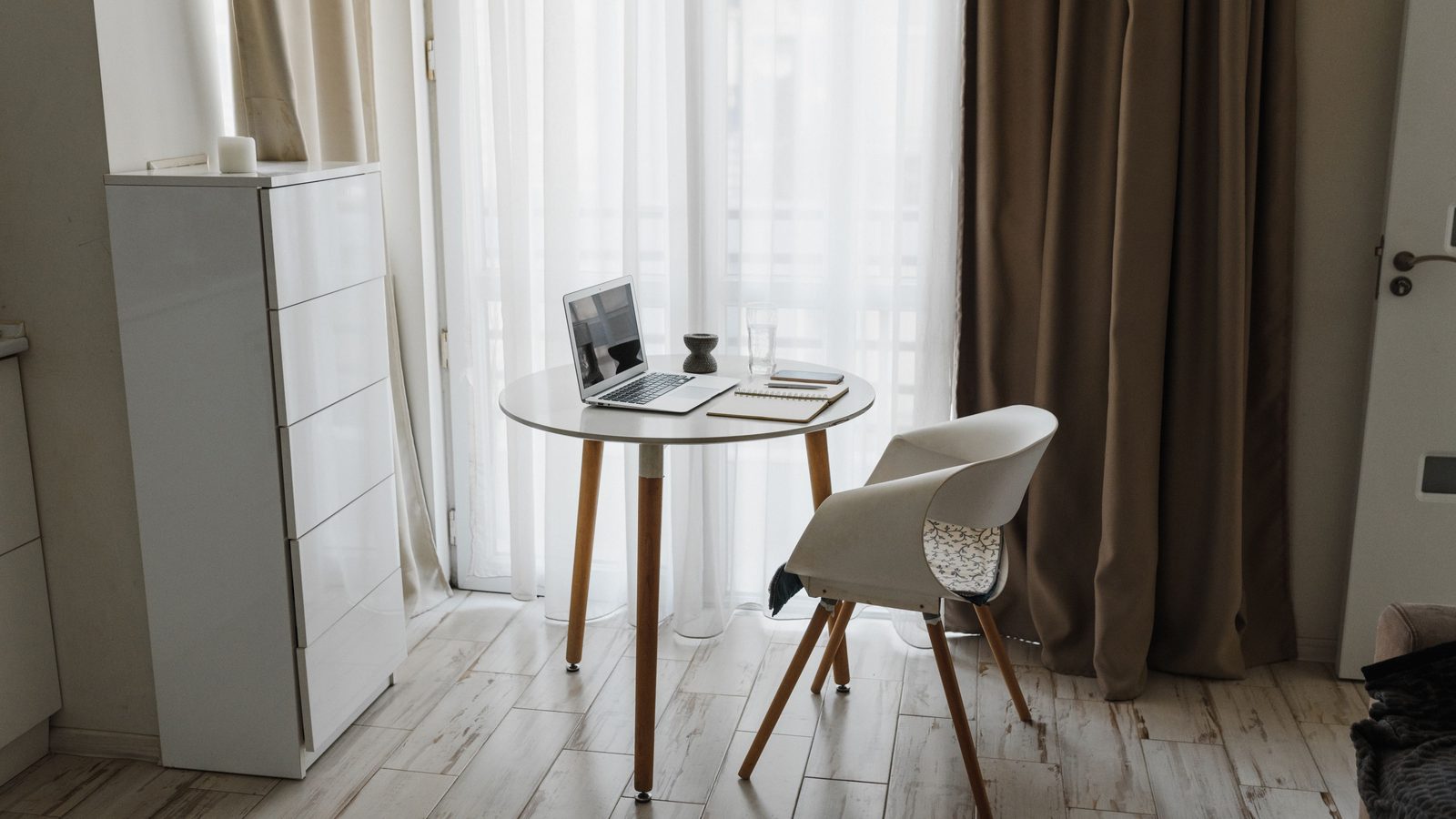 Small round table with a laptop and a notebook in front of a sheer curtain, atmosphere photo, not a product pick