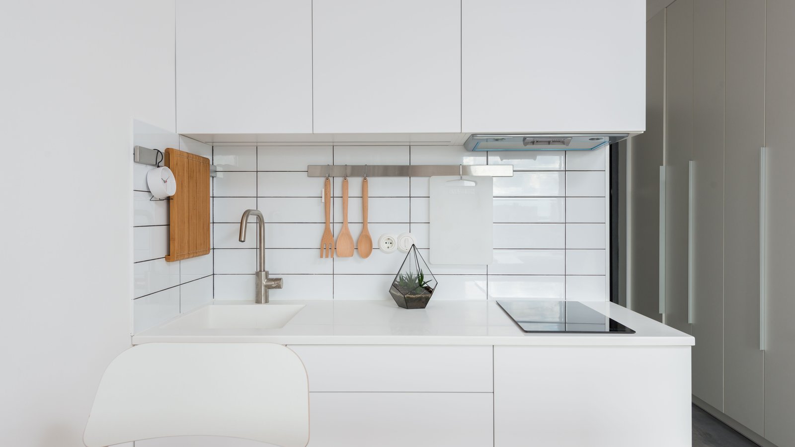 Compact white kitchen with a short run of cabinets, a tiled backsplash and a cooktop, atmosphere photo, not a product pick